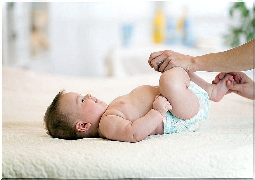 Baby lying on his back moves his legs with the help of an adult.